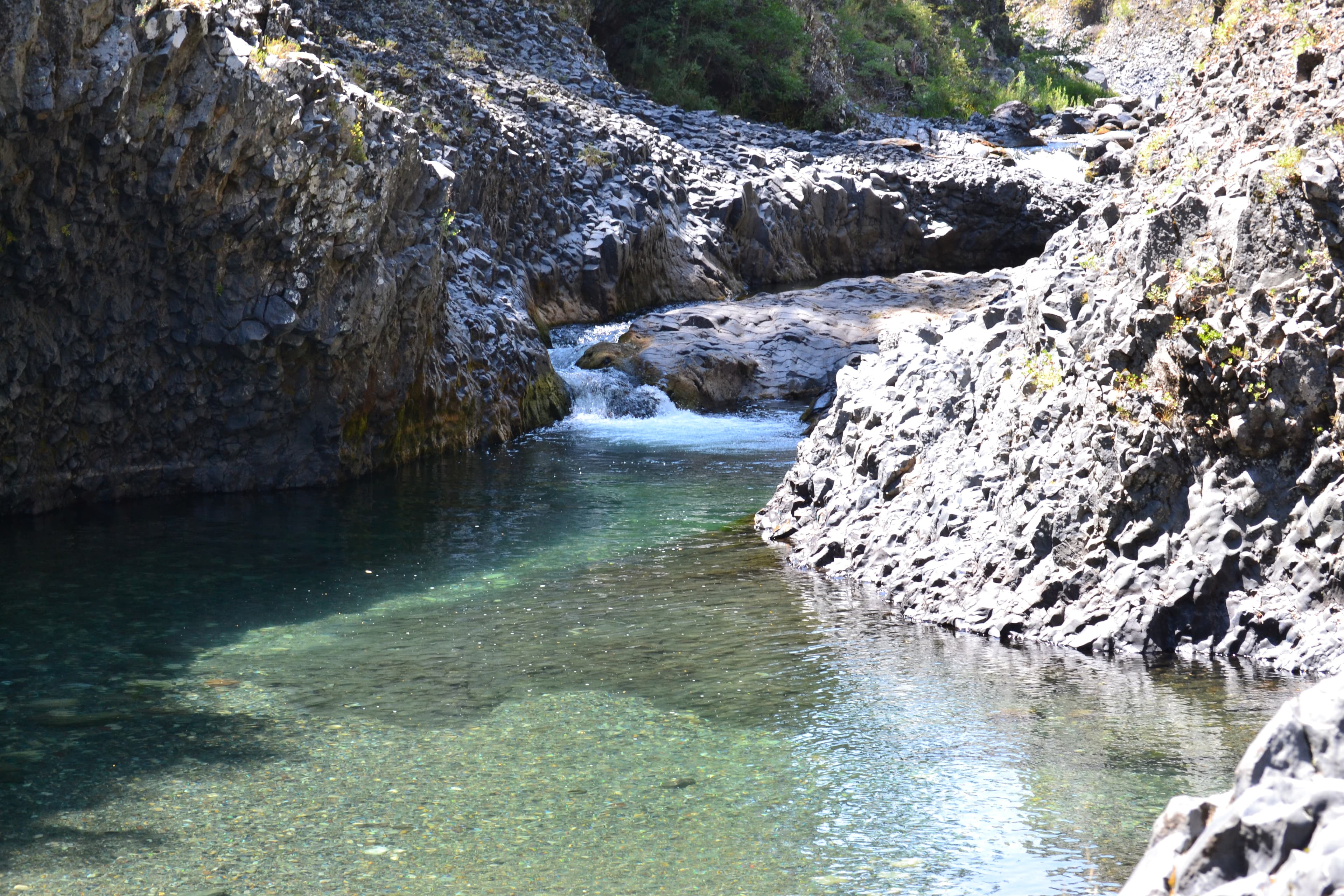 Poza de agua turquesa y transparente encajonada entre rocas de basalto